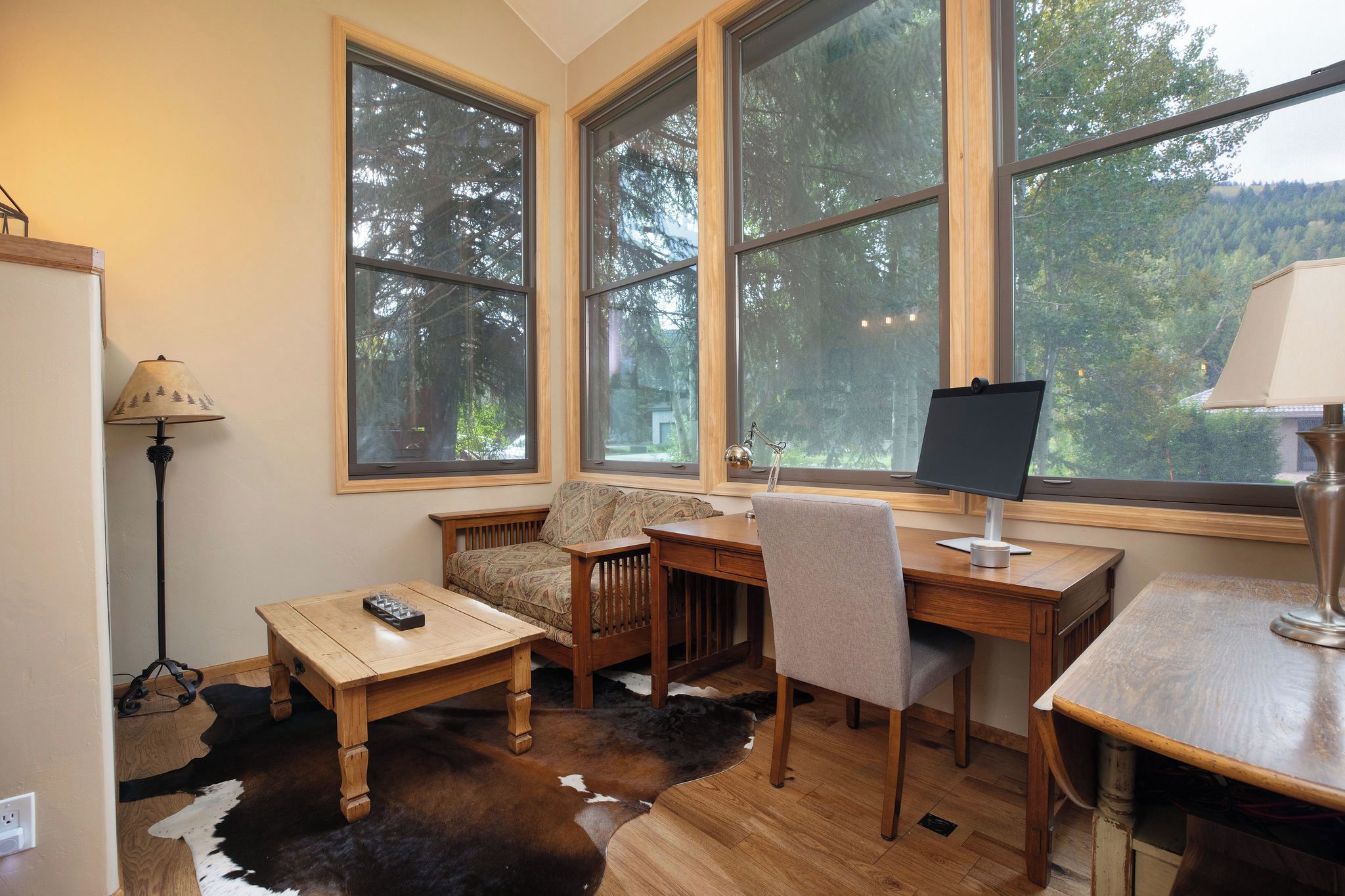 A room with a large window, a desk, a chair, a sofa, and a lamp.