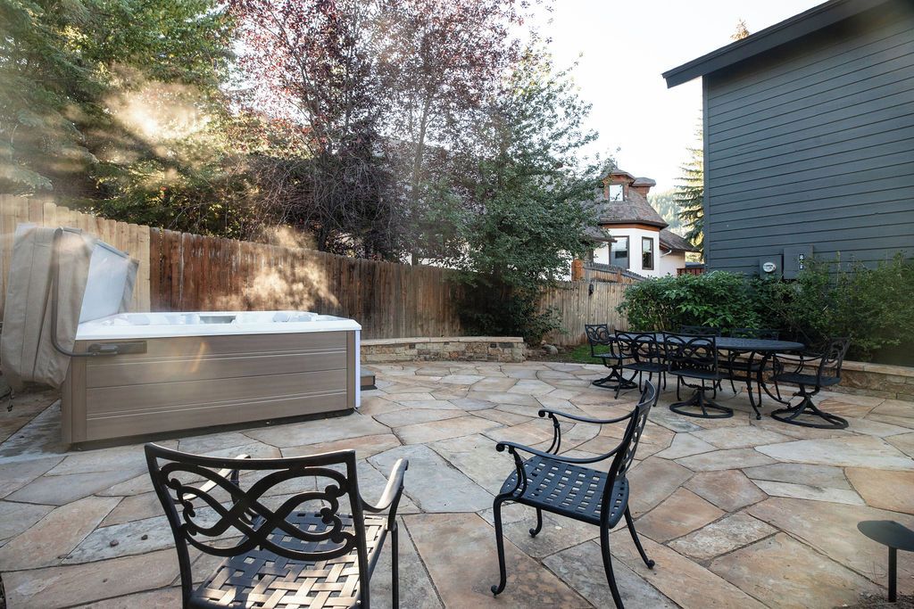 Un espace extérieur aménagé en terrasse, avec un sol en pierre, un jacuzzi et des meubles de jardin en métal.