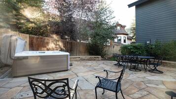 Un espace extérieur aménagé en terrasse, avec un sol en pierre, un jacuzzi et des meubles de jardin en métal.