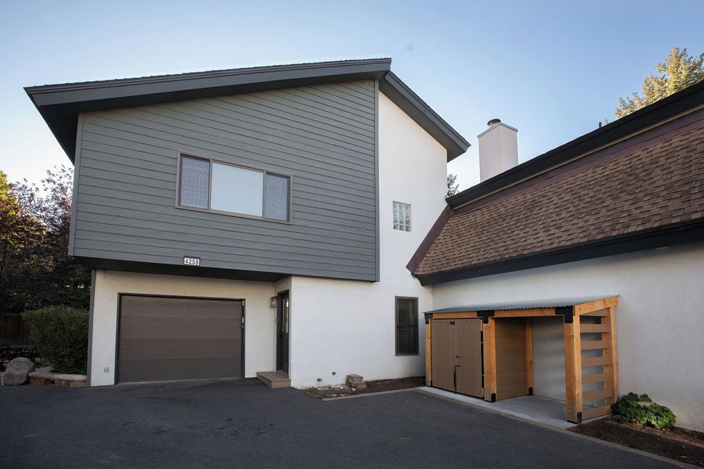 Ein modernes, zweistöckiges Haus mit Garage und einer überdachten Holzkonstruktion, bewölkter Himmel.
