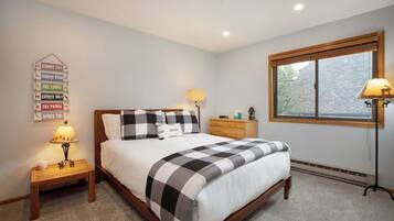 A bedroom with a bed, bedside tables, a lamp, a dresser, a window with blinds, and a wall sign.