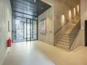 Ein modernes Interieur mit Treppe, Feuerlöscher und Glastür zum Außenbereich.