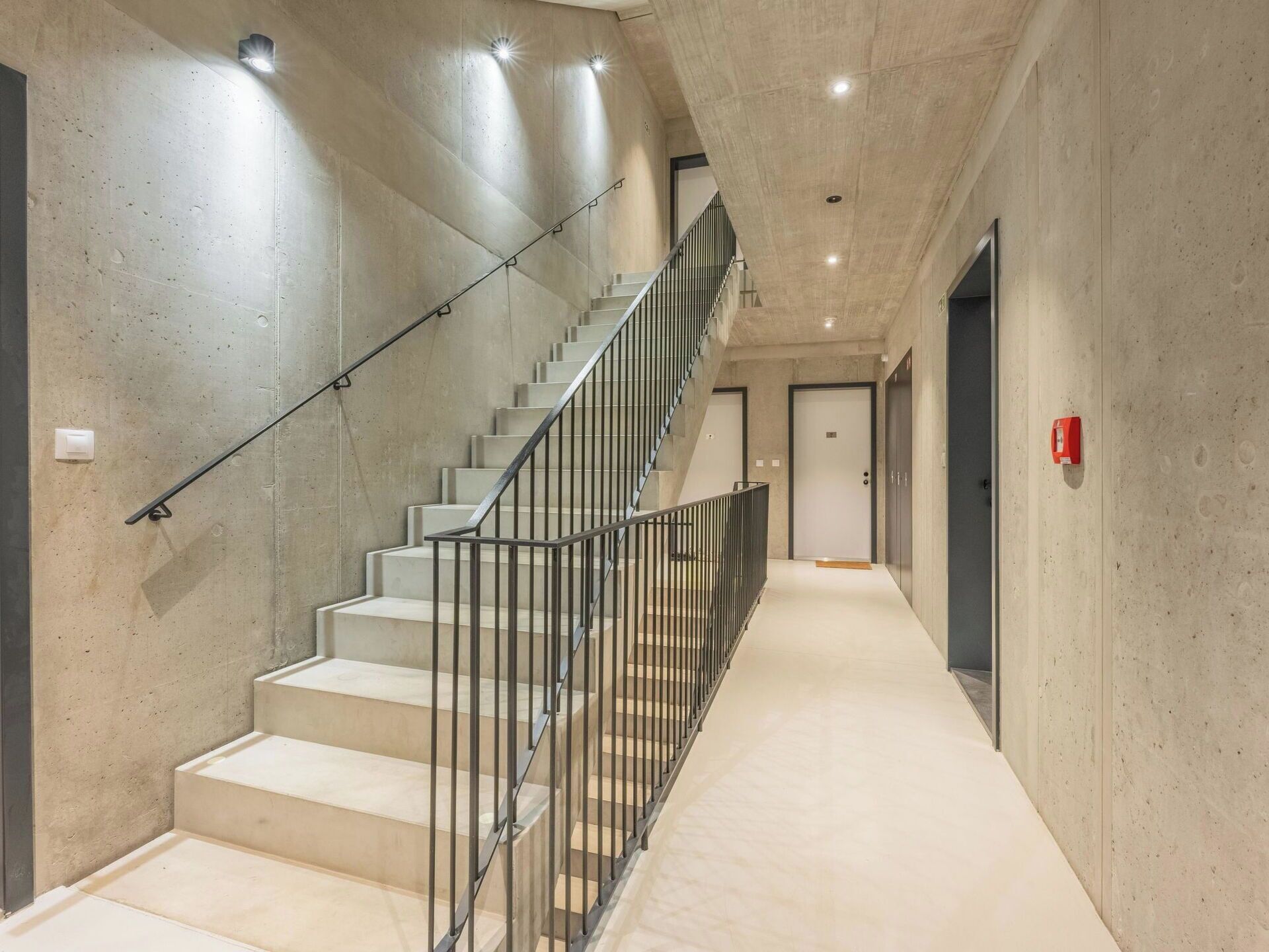Ein modernes Interieur mit einer Betontreppe und einem geraden Flur, der zu einer Tür führt.