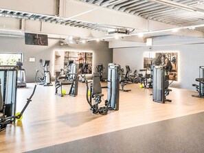 Een sportschool met diverse fitnessapparaten, een houten vloer en een hoge ruimte met zichtbare balken.