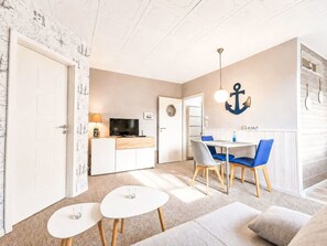 Ein kompakter Wohnbereich mit Küchenzeile, einem Essbereich mit blauen Stühlen und einer gemütlichen Sitzecke mit Sofa und zwei kleinen Tischen.