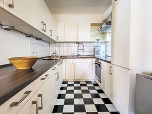 Une cuisine moderne avec des meubles blancs, un carrelage noir et blanc à motifs, un grand saladier doré et un four encastré.