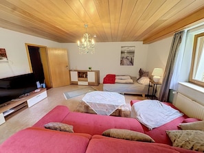 Ein Wohnzimmer mit Sofa, Fernseher, einer Lüster, einem Gemälde und einem Fenster mit Vorhängen.