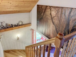 A wooden staircase with a railing, a wall-mounted shelf with various metal items, and a large forest-themed painting.