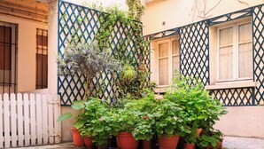 Un patio con plantas en macetas, cerca de piquetes blanca y un edificio con diseño de celosía.