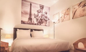 Une chambre d’hôtel comprenant un lit, une lampe et des œuvres d’art murales, notamment une statue et un tableau représentant des fleurs.