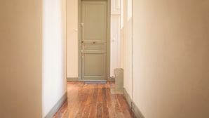 Un pasillo estrecho con piso de madera y una puerta verde al final.