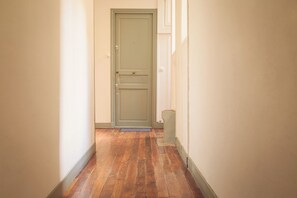 Un couloir étroit, avec un plancher en bois et une porte verte au fond.