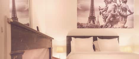 Habitación de hotel con cama, mesita de noche, lámpara y una pared con una imagen de la Torre Eiffel y una estatua.