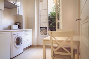 Une cuisine compacte équipée d’un lave-linge, d’une machine à café et d’une fenêtre donnant sur un espace verdoyant.