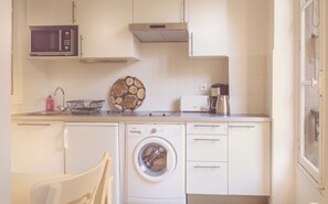 Une cuisine compacte équipée d’un lave-linge, d’un four à micro-ondes et d’une machine à café.