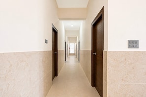 A hallway with doors on both sides, a light switch, and a window at the end. - Collection O Magadi Road Metro (Nelamangala)