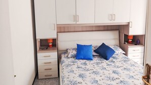 Et soveværelse med seng, to puder, et natbord, en lampe og et klædeskab.