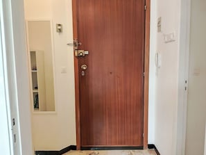 A wooden door with a latch, a small shelf with a mirror, and a light switch on the wall. - Cosy apartment for 2 guests with A/C, WIFI, TV and balcony (Loano)