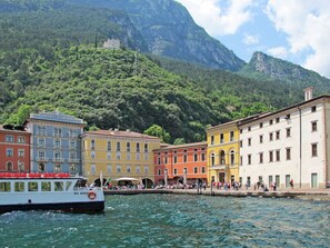 Un hôtel situé au bord de l’eau, avec des bâtiments aux couleurs vives, un bateau amarré au premier plan et une chaîne de montagnes en arrière-plan.