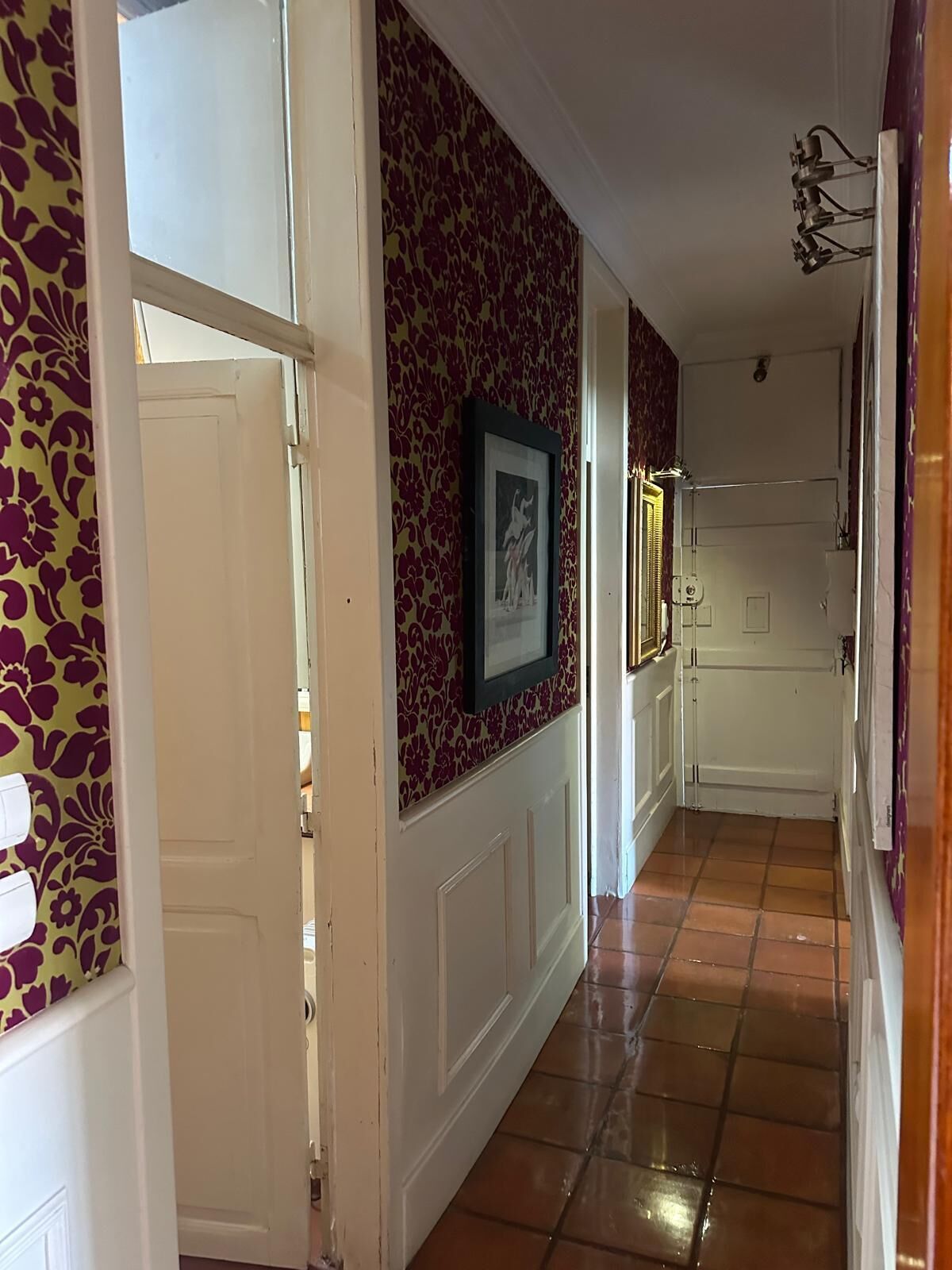 A hallway with patterned wallpaper, a framed picture, and a tiled floor.