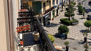 A balcony with outdoor furniture, a view of a street with parked cars, and a row of buildings with balconies. - Refined structure in Milazzo, designed to experience an exclusive stay. (Milazzo)