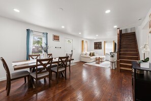 Amplia sala de estar con mesa y sillas de comedor, sofá, escalera y vistas al exterior.