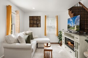 Una sala de estar con un sofá modular, una chimenea, un televisor y una ventana con cortinas.