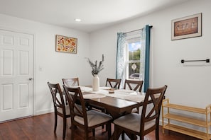A dining room with a wooden table and chairs, a vase with plants, and artwork on the walls. - New & Cozy 3BR Retreat | Sleeps 6 | Free Parking ! (Alexandria)