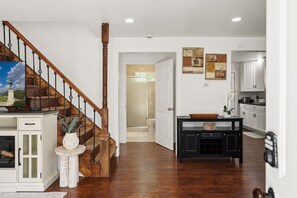 A spacious living area with a wooden staircase, a kitchen with white cabinets, and artwork on the walls. - New & Cozy 3BR Retreat | Sleeps 6 | Free Parking ! (Alexandria)