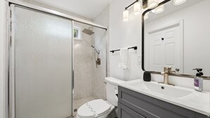 Et badeværelse med brusebad, toilet, vask og spejl.