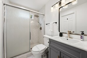 Un baño con ducha, inodoro, lavamanos y espejo.