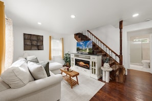 A living room with a fireplace, a sofa, a coffee table, and a television. - New & Cozy 3BR Retreat | Sleeps 6 | Free Parking ! (Alexandria)