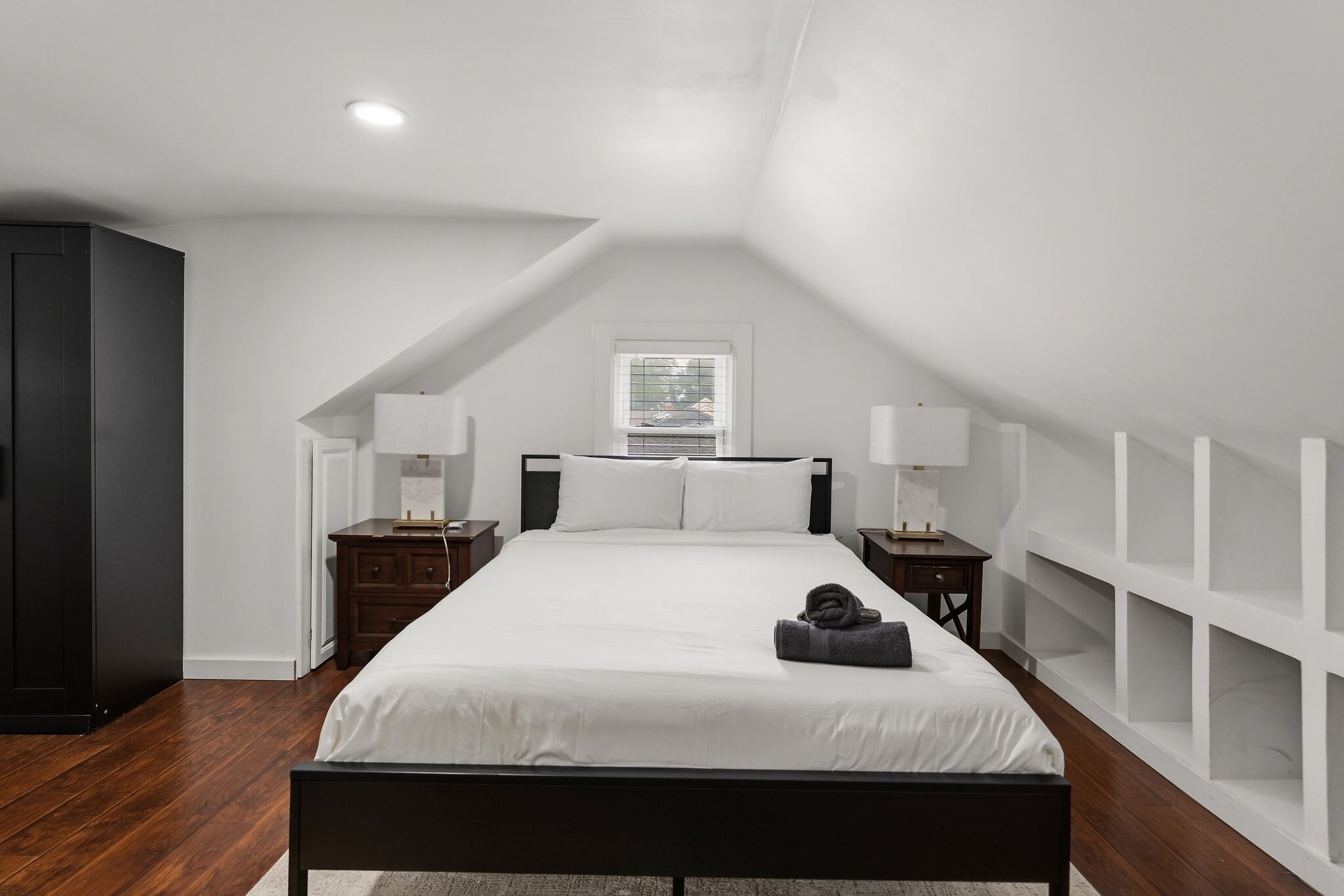Een slaapkamer met een groot bed, twee nachtkastjes, een kledingkast en een raam met jaloezieën.