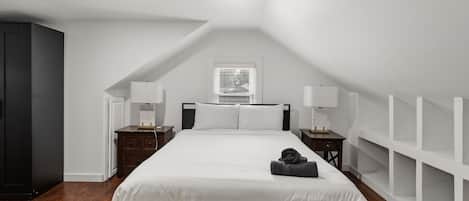 A bedroom with a large bed, two bedside tables, a wardrobe, and a window with blinds.