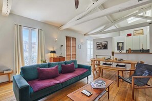 Ein Wohnzimmer mit einem türkisfarbenen Sofa, einem Holztisch und einem Essbereich mit Holztisch und Stühlen.