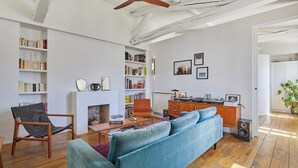 Una sala de estar con sofá, sillón, chimenea, estanterías y un escritorio con computadora.