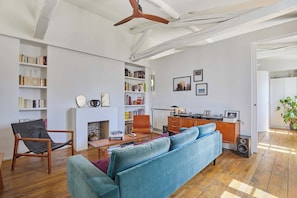 Ein Wohnzimmer mit einer Couch, einem Sessel, einem Kamin, Bücherregalen und einem Schreibtisch mit einem Computer.