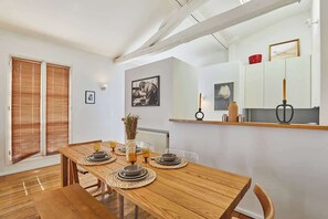 A dining area with a wooden table set for four, a vase with dried flowers, and a framed picture on the wall. - Apartment in the heart of Le Marais (Paris)