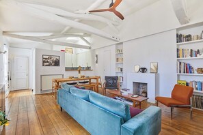 A living room with a wooden ceiling, a blue sofa, a wooden dining table, and a bookshelf. - Apartment in the heart of Le Marais (Paris)