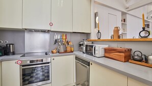 Una cocina compacta con horno empotrado, microondas y lavavajillas, que presenta un piso con estampado de cuadros y un caja de almacenamiento de madera.