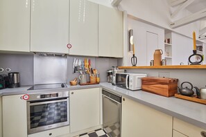 Eine kompakte Küche mit Einbauofen, Mikrowelle und Geschirrspüler, mit einem Schachbrettmuster auf dem Boden und einer Holzaufbewahrungsbox.