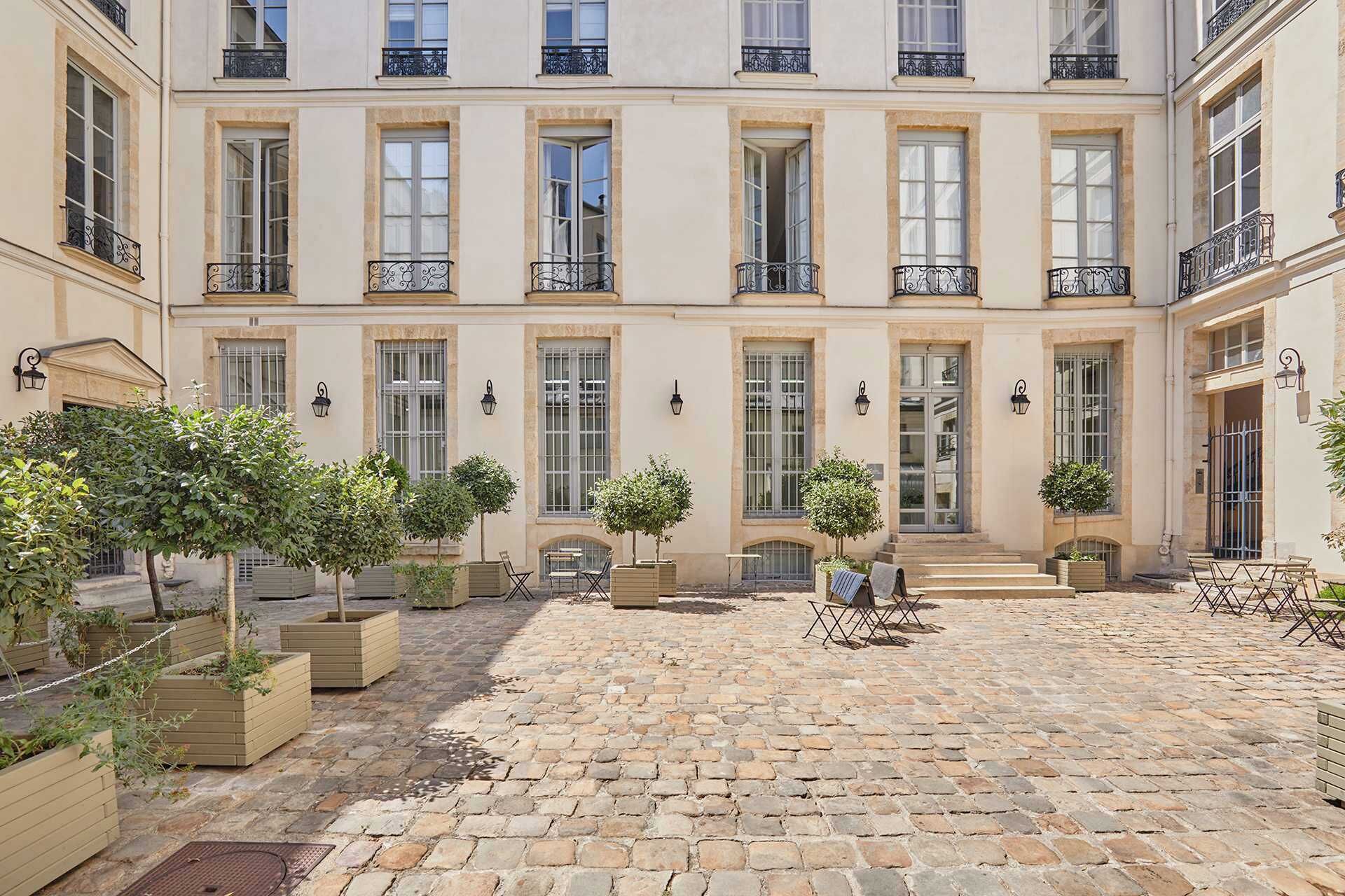 A courtyard with a cobblestone floor, multiple windows, and outdoor seating.