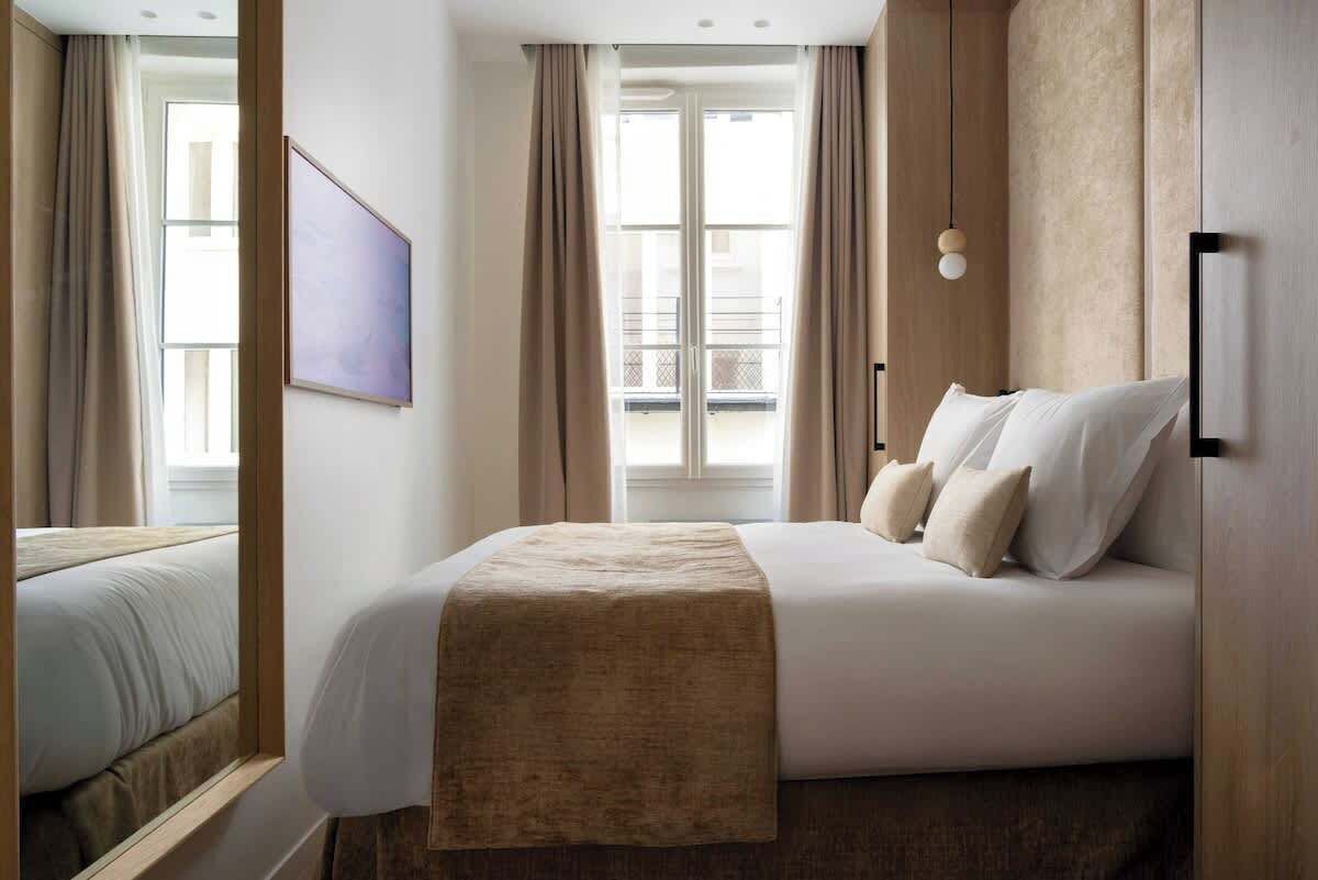 Une chambre d’hôtel avec un grand lit, une table de chevet, un téléviseur fixé au mur et une fenêtre avec des rideaux.
