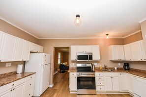 A kitchen with white cabinets, a refrigerator, a microwave, an oven, and a coffee maker. - Peaks & Paws -Pet friendly, single level, sleeps 8 close to beach (Conway)