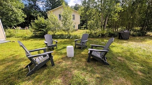 A backyard with four Adirondack chairs, a small round table, and a house in the background. - Peaks & Paws -Pet friendly, single level, sleeps 8 close to beach (Conway)