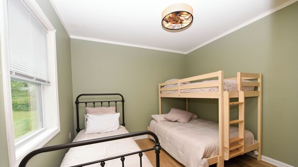 Quarto com uma cama de solteiro, uma cama beliche e uma janela com persianas.