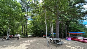 Um camping com mesas de piquenique, espaço para guardar canoas e terreno de terra.