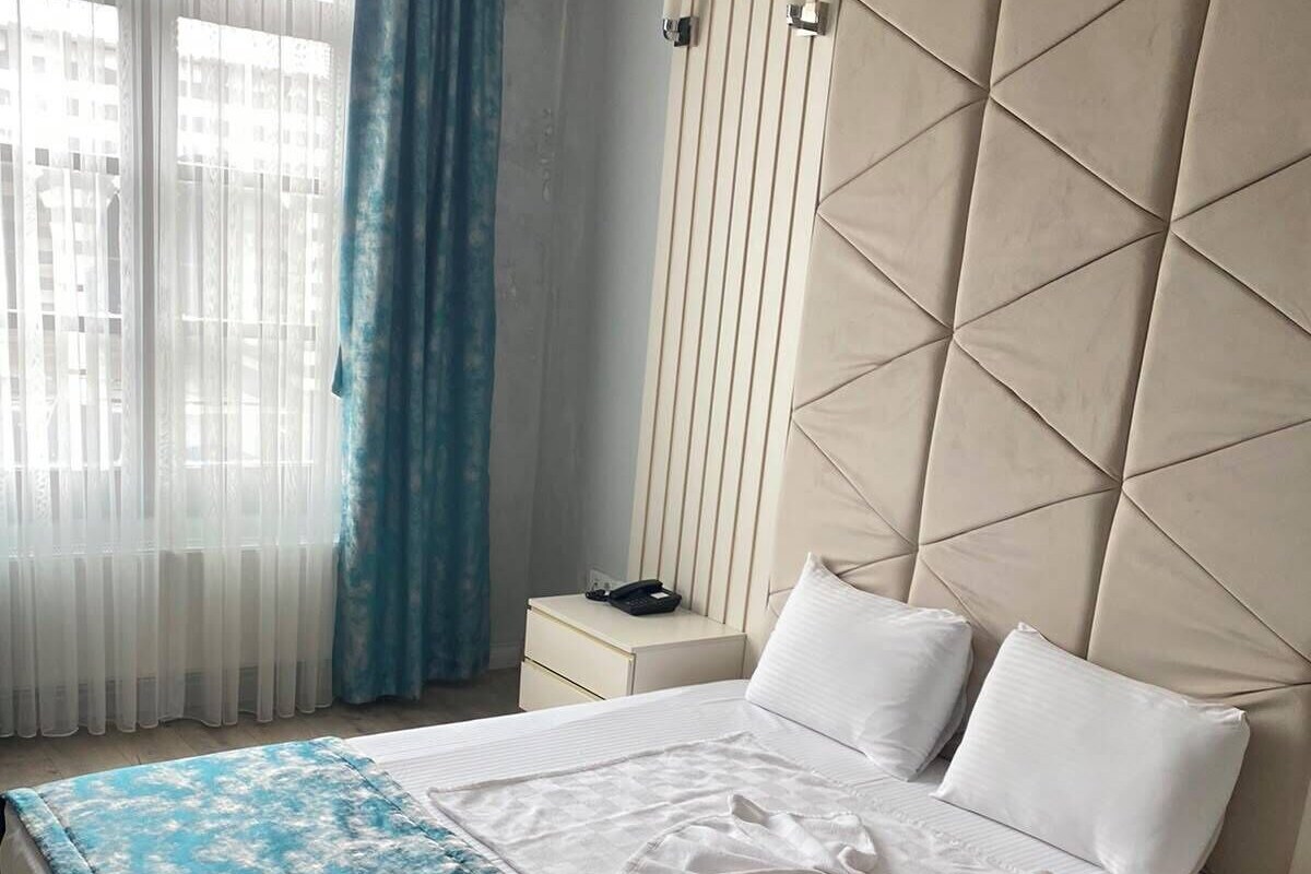 Ein Hotelzimmer mit einem Bett, Nachttischen, einem blauen Vorhang und einem Fenster mit Jalousien.