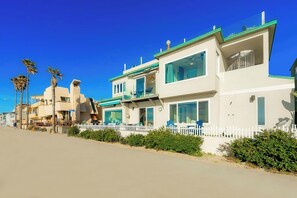 Ein Strandgrundstück mit weißer Fassade, mehreren Balkonen und einem weißen Zaun.