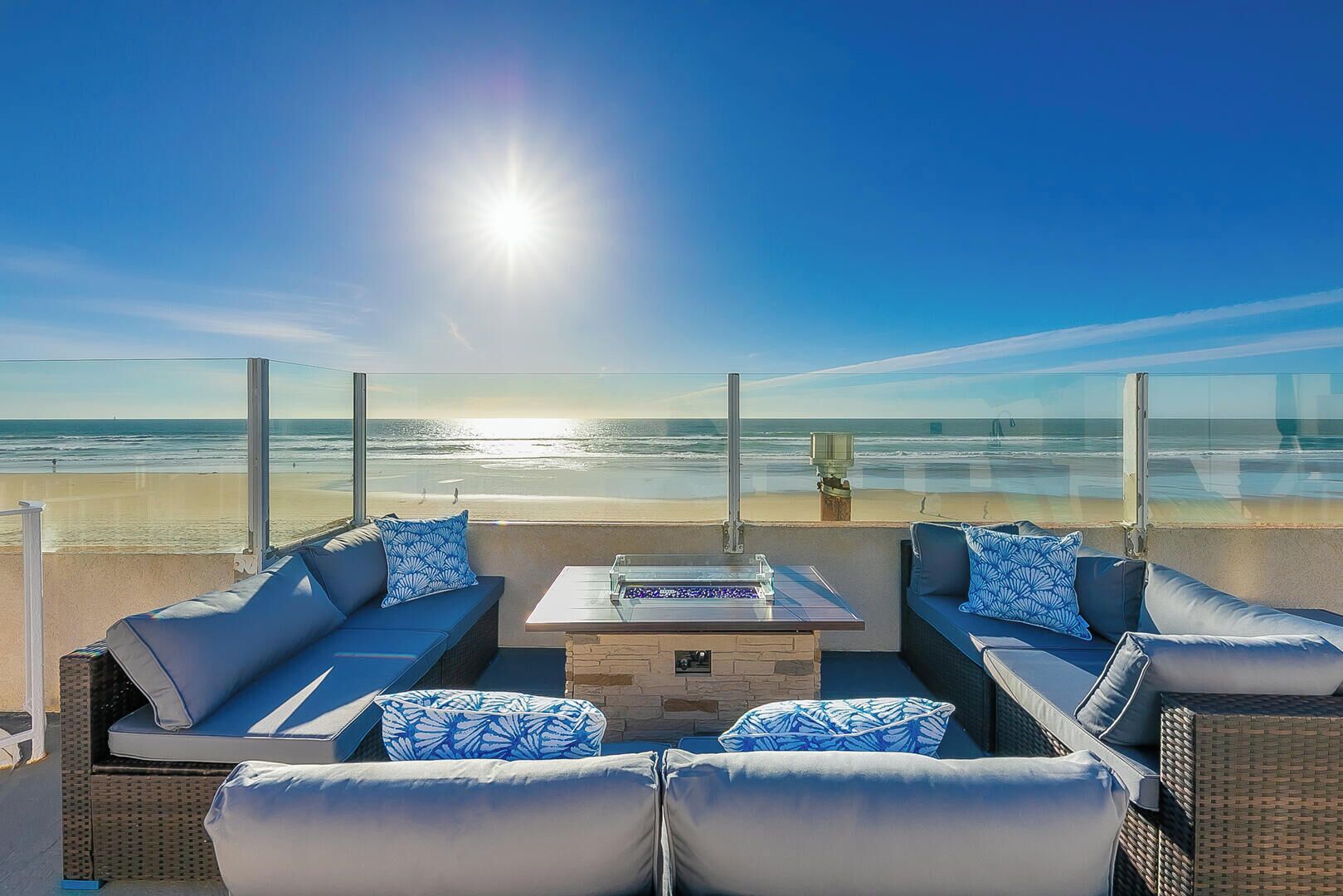 Eine Terrasse direkt am Strand mit zwei Sofas, einem Tisch und Blick auf das Meer.